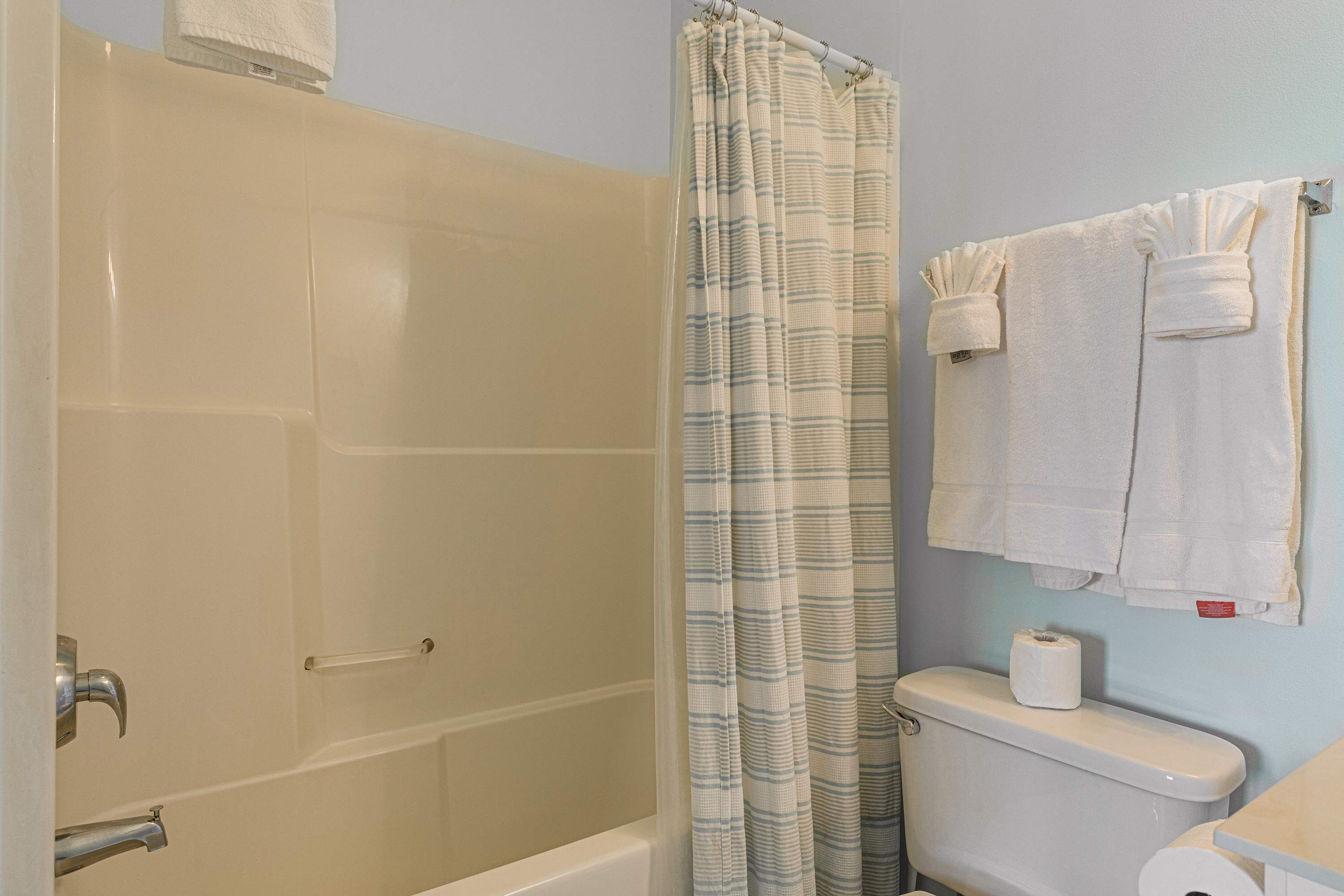 A bathroom with a bathtub, a shower curtain, a toilet, and a towel rack.