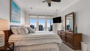 A bedroom with a bed, a dresser, a television, and a large window.