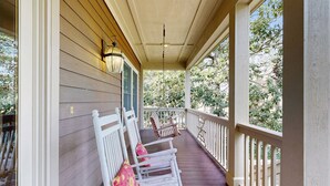 A covered porch with wooden railings and a bench with cushions. - Spacious home with pool - walk to beach & golf (Kiawah Island)