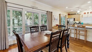 A dining area with a large wooden table and chairs, a kitchen area with a refrigerator and cabinets, and large windows with curtains. - Spacious home with pool - walk to beach & golf (Kiawah Island)