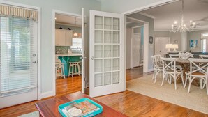A spacious living area with a wooden floor, a dining table with white chairs, and a chandelier. - Elegant home on the boardwalk with 2 balconies & shared pools - walk to beach (Isle of Palms)