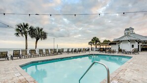A pool area with lounge chairs, palm trees, and a building with a metal roof. - Elegant home on the boardwalk with 2 balconies & shared pools - walk to beach (Isle of Palms)