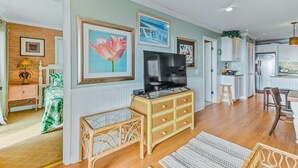 A spacious living room with a television, wicker furniture, and artwork on the walls. - Oceanfront, event-friendly home with multiple decks & WiFi - 2 dogs ok (Folly Beach)