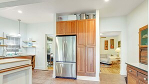 A modern kitchen with stainless steel appliances, wooden cabinets, and a dining area with a table and chairs. - One Block to the Beach Cute Home w/ Deck, Garden Patio, Central AC & WiFi (Folly Beach)