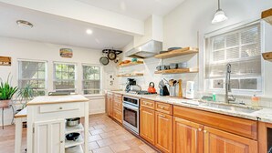 A modern kitchen with wooden cabinets, a central island, and a large window. - One Block to the Beach Cute Home w/ Deck, Garden Patio, Central AC & WiFi (Folly Beach)