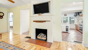 A living room with a fireplace, wooden flooring, and a television mounted above it. - One Block to the Beach Cute Home w/ Deck, Garden Patio, Central AC & WiFi (Folly Beach)