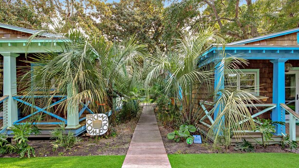 A wooden pathway leading to two blue-roofed structures surrounded by lush greenery. - Trio of coastal cottages with private courtyard, full kitchens, & WiFi - dogs ok (Folly Beach)