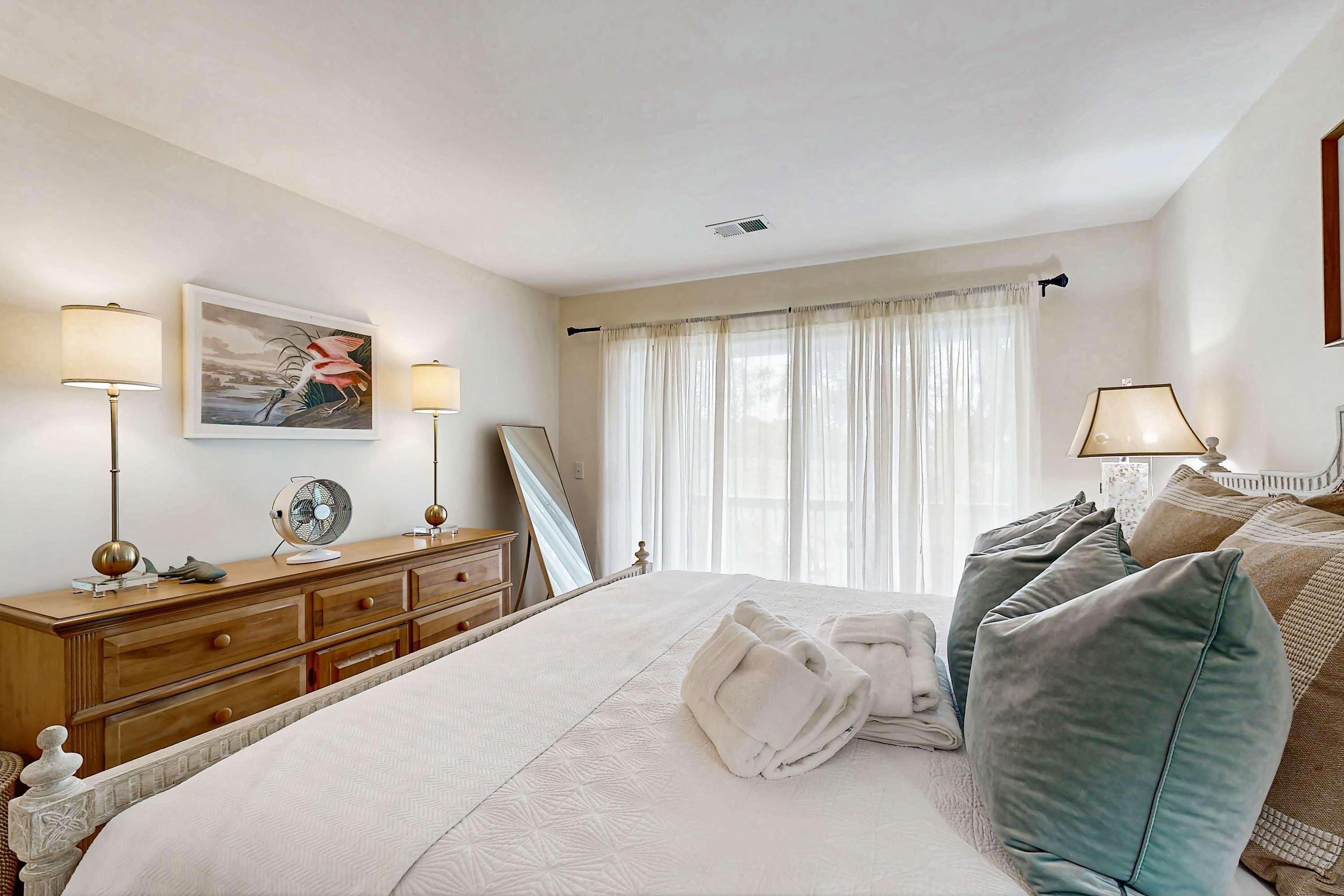 Ein Hotelzimmer mit einem großen Bett, einer Holzkommode, einem Spiegel und einem Fenster mit Vorhängen.