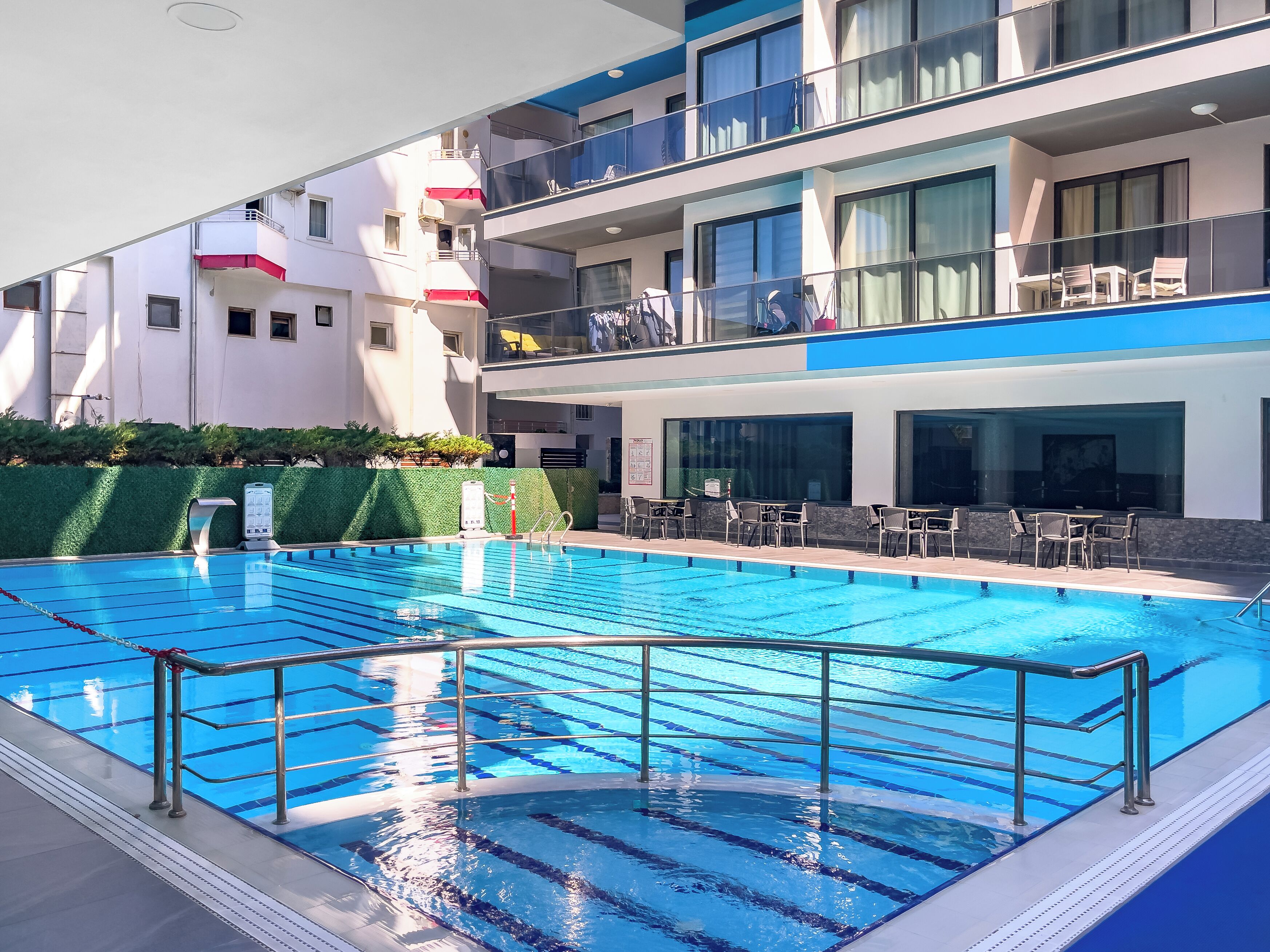 A swimming pool with clear blue water, surrounded by a modern building with balconies and outdoor seating.