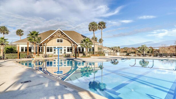 A large swimming pool with clear blue water, surrounded by palm trees and a building with a tiled roof. - Charming Island Getaway with a Furnished Deck Offering Forest & Fairway Views (Seabrook Island)
