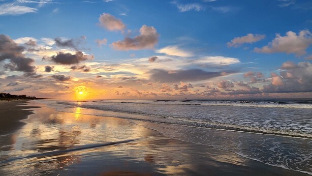 Ein Strand mit Sonnenuntergang, Wellen und klarem Himmel.