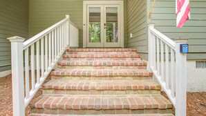 Eine Treppe aus Ziegelsteinen mit weißen Geländern führt zu einer Tür mit Fensterfeldern.