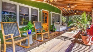 A covered porch with wooden flooring, two rocking chairs, a small table, and potted plants.