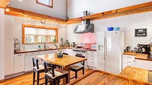 A kitchen with white brick walls, wooden beams, a central island with chairs, a stove, and a refrigerator.