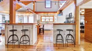 A spacious kitchen with wooden beams, a central island with stools, and a view to the dining area.