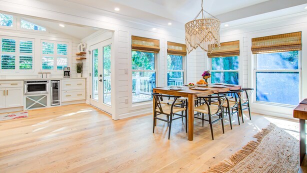 Una cocina amplia con armarios blancos, una mesa de comedor de madera y ventanas grandes con persianas.