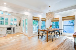 A spacious kitchen with white cabinetry, a wooden dining table, and large windows with blinds. - Stunning home, close to beach with large deck, pool & outdoor shower (Isle of Palms)