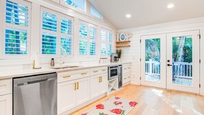 Una cocina moderna con armarios blancos, electrodomésticos de acero inoxidable y ventanas amplias.
