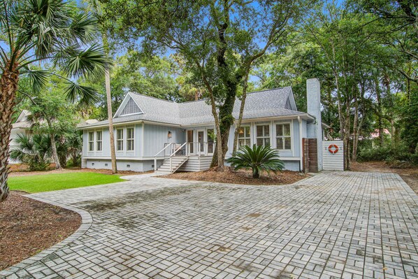 A two-story house with a brick pathway leading to the entrance, surrounded by trees and a well-maintained lawn. - Stunning home, close to beach with large deck, pool & outdoor shower (Isle of Palms)