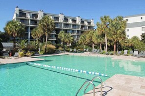 A hotel with a swimming pool surrounded by palm trees and lounge chairs.