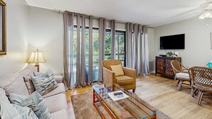 Ein Wohnzimmer mit einer Couch, einem Sessel, einem Couchtisch und einem Fernseher auf einem Schrank.