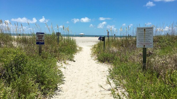 Un sendero en la playa con letreros que dicen 'No transite por las dunas' y 'Bienvenido a nuestra playa'.