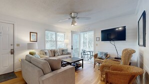 Una sala de estar con sofá, mesa de centro, sillas de mimbre, televisor y ventilador de techo.