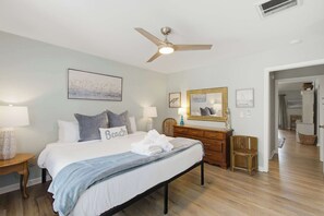 Ein Hotelzimmer mit Bett, Deckenventilator, Nachttisch mit Lampe, Kommode und Spiegel.
