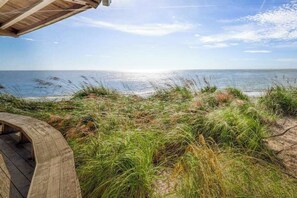 A wooden deck overlooking a beach with dunes and the ocean in the background.