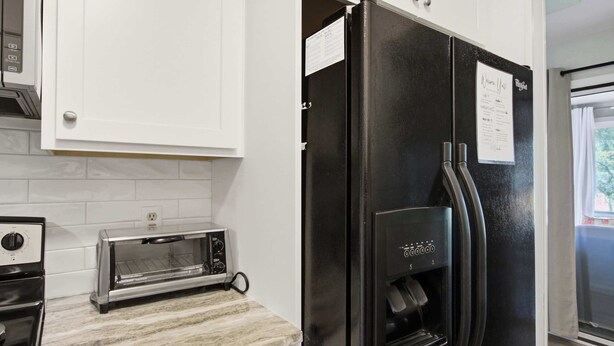 Una cocina con armarios blancos, un refrigerador negro con una nota, un tostador y una estufa.