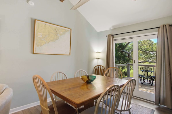 A dining area with a wooden table, six chairs, a map on the wall, and a view of the outdoors through a glass door.