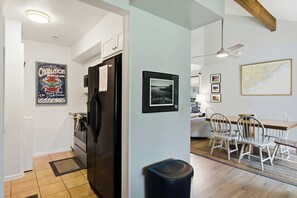 A modern kitchen with a black refrigerator, a dining area with white chairs, and a ceiling fan.