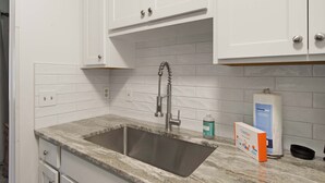 Una cocina con armarios blancos, un lavamanos de acero inoxidable y una encimera de mármol.