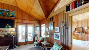 Et hyggeligt værelse med trævægge og -loft, en seng, et skrivebord med lampe, en stol og en ventilator.