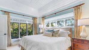 A bedroom with a large bed, a nightstand, a lamp, and a window with curtains.