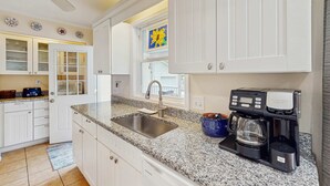 A kitchen with white cabinets, a granite countertop, a coffee maker, and a window with a yellow artwork.