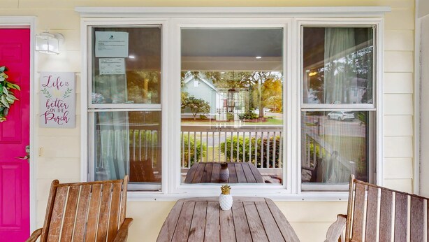 A porch with a wooden table and two chairs, a pink door, and a sign that says "Life is better on the porch."
