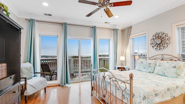 Une chambre à coucher avec un lit, une chaise, une commode, un ventilateur de plafond et une vue par la fenêtre.