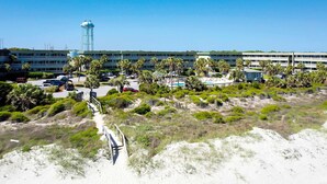 A coastal hotel with a parking lot, palm trees, and a water tower. - Beachfront condo with pool, beach access, pier, private balcony, & central AC (Isle of Palms)