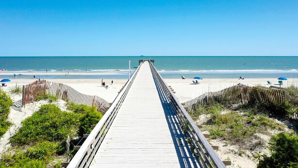 A wooden boardwalk leading to a beach with umbrellas and people. - Beachfront condo with pool, beach access, pier, private balcony, & central AC (Isle of Palms)