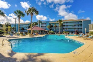 A hotel with a swimming pool, palm trees, and a clear blue sky.