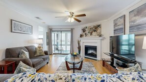 A modern living room with a sofa, TV, fireplace, and a glass coffee table. - Elegant riverfront condo with access to private W/D, central AC, and pool access (Folly Beach)