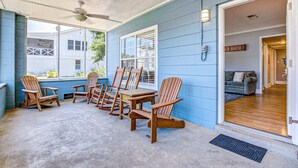 En overdækket veranda med Adirondack-stole og et bord, en blå facade og et skilt med teksten "CH-HOUSE".