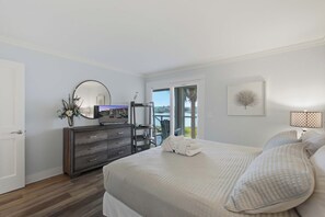 A bedroom with a bed, a dresser, a mirror, a television, and a window with a view of the outdoors. - First-floor villa w/ magnificent river view & community pool/dock/tennis courts (Folly Beach)