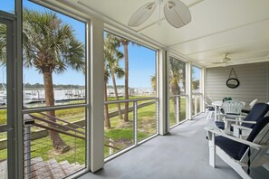 Een overdekt terras met uitzicht op een jachthaven en palmbomen.