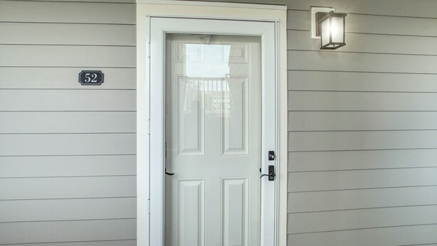 A white door with a number '52' sign above it, a light fixture to the right, and horizontal siding on the wall. - First-floor villa w/ magnificent river view & community pool/dock/tennis courts (Folly Beach)