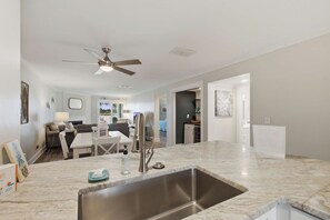 A modern kitchen with a stainless steel sink, a ceiling fan, and a dining area with a table and chairs. - First-floor villa w/ magnificent river view & community pool/dock/tennis courts (Folly Beach)