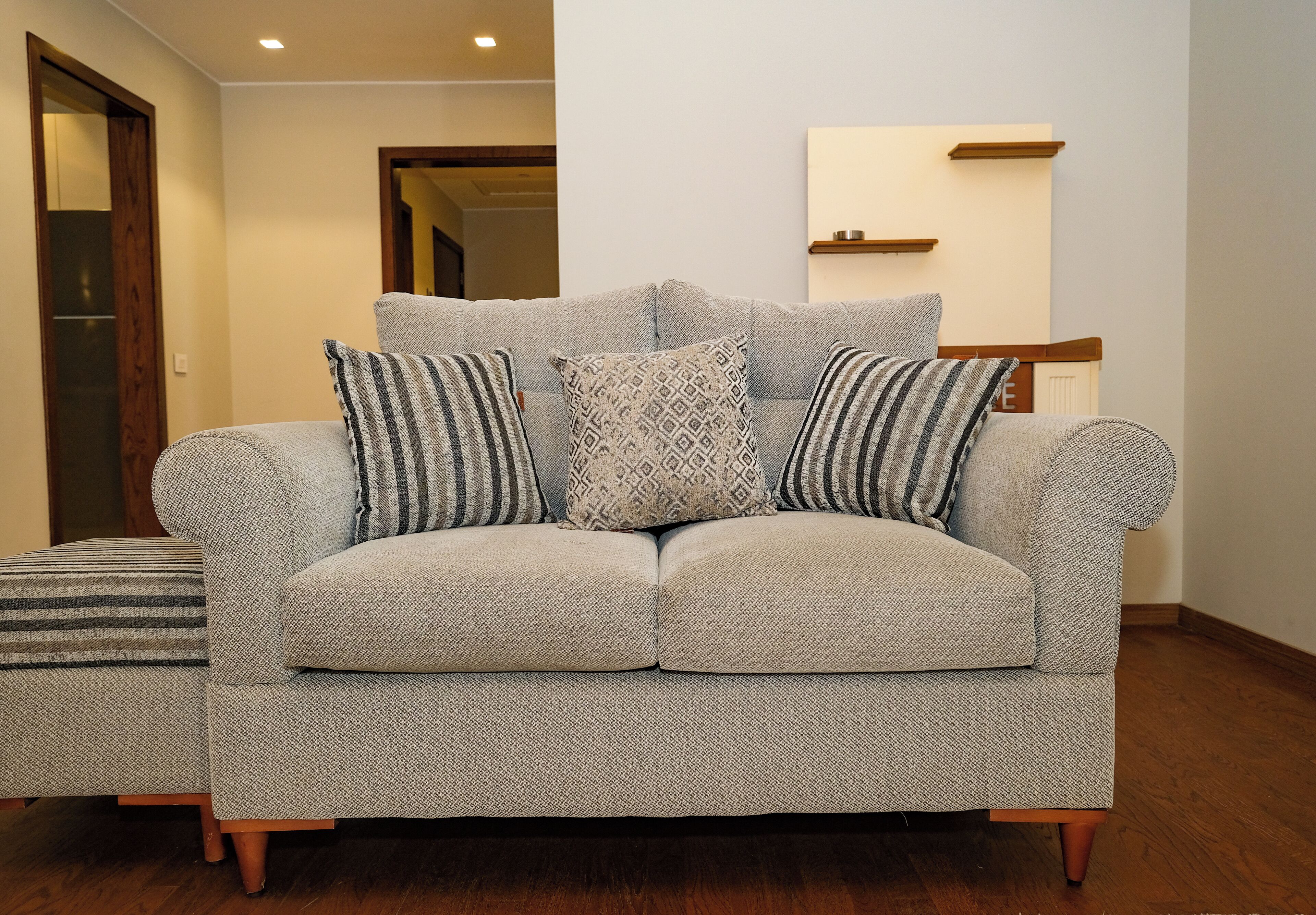 A grey sofa with patterned cushions in a room with wooden flooring and a wooden door.