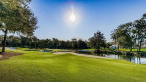 Golfkenttä, jossa on lampi, puita ja kirkas taivas.