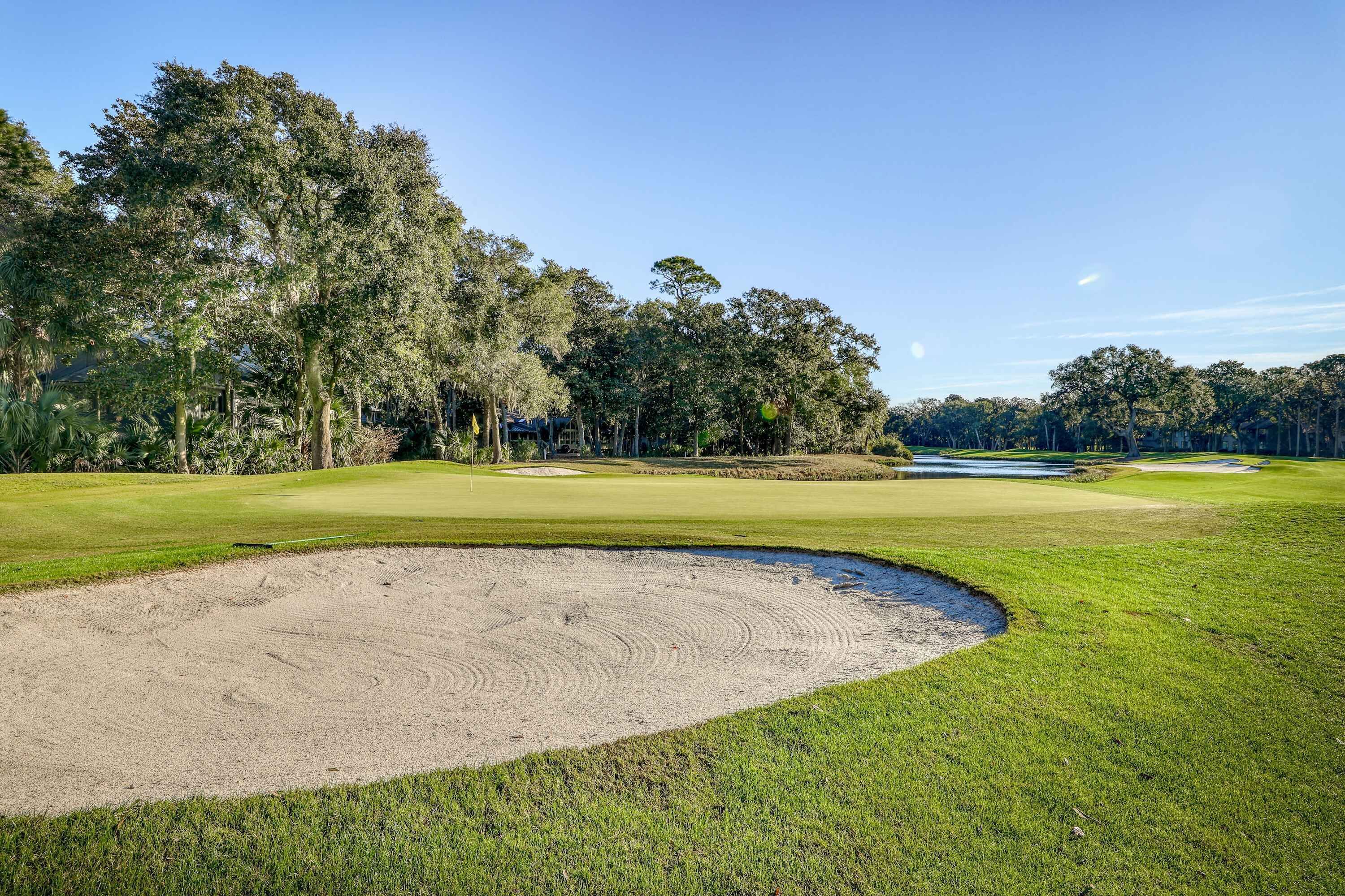Un parcours de golf doté de bunkers de sable, d’une pelouse bien entretenue et de grands arbres en arrière-plan.